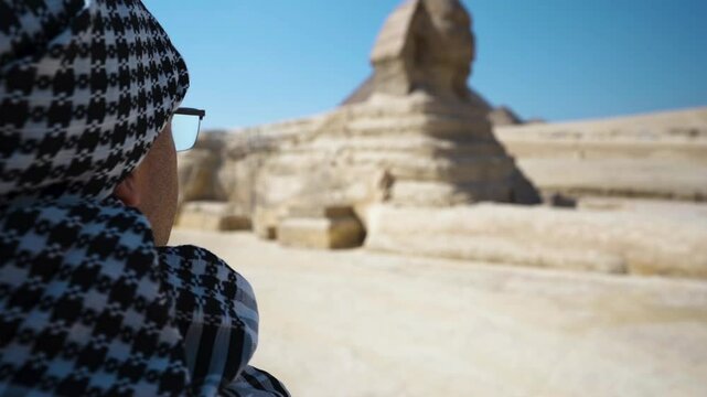 A man in a keffiyeh looks at a sphinx, a mythical creature that guards the afterlife