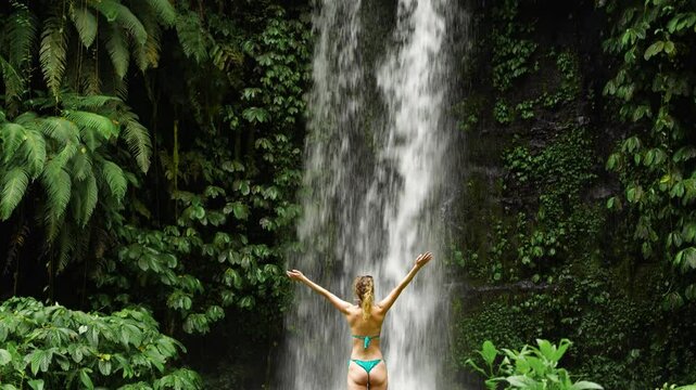 Woman in bikini standing under tropical waterfall in the jungle of Indonesia