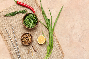 Wooden bowl with fried maggots, arugula, lemon and green onion on beige background