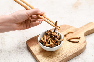 Female hand with chopsticks and bowl of fried maggots on white background