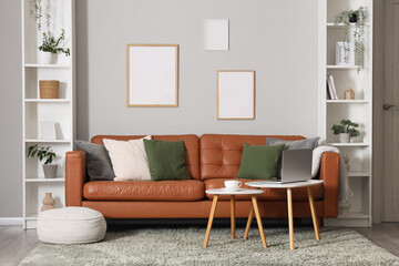Interior of living room with shelving unit, stylish leather sofa and laptop on coffee table near white wall