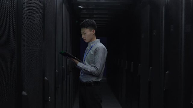 Male Professional Worker IT administrator In Engine Control server Room among rows of rack server cabinets and using laptop to check its work
