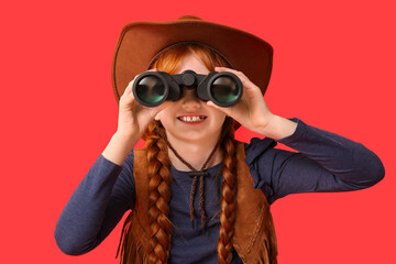 Cute happy teenage girl in cowboy hat with binoculars on red background