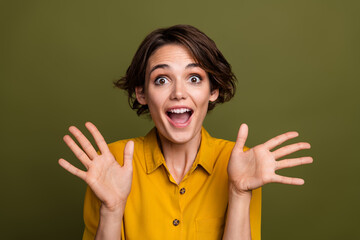 Smiling young woman in casual yellow blouse showing excited gestures against a khaki background,...