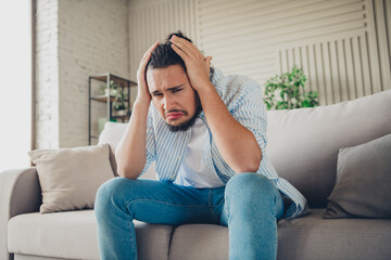 Obraz premium Young man showing stressed emotions while sitting on a couch in a bright and stylish living room interior