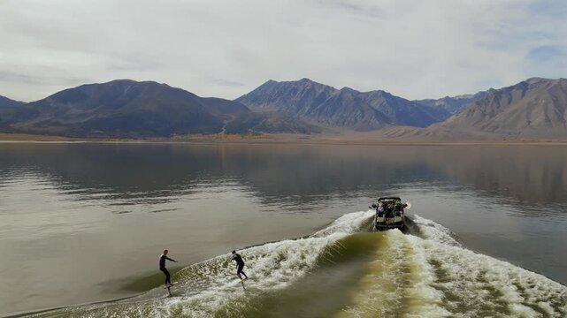 Wake foil surf surfing surfers water sports MB boat left side wave Lake Crowley Mammoth Mountain Lakes California aerial drone golden still calm water morning cloudy autumn follow forward motion