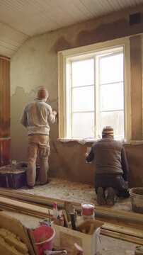 Slider shot of two men plastering walls with clay, home improvement, vertical