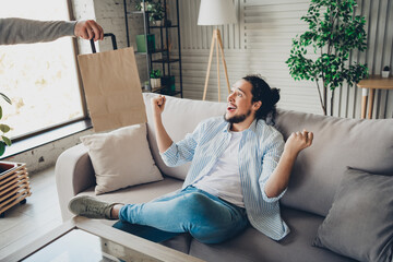 Fototapeta premium Young man relaxing on couch receives delivery, excited in bright living room