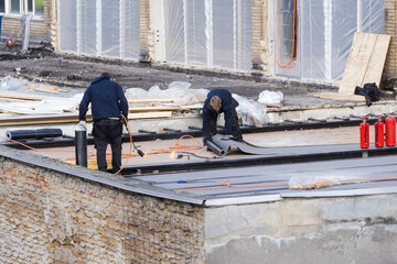 Workers installing waterproofing membrane and asphalt bitumen shingle on flat roof © brizmaker