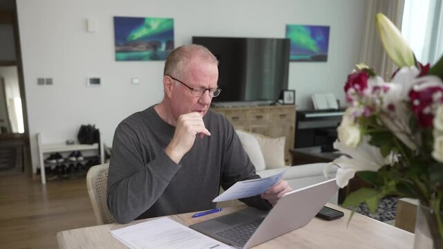 Senior man trying to do his own taxes or finances on a laptop computer at home