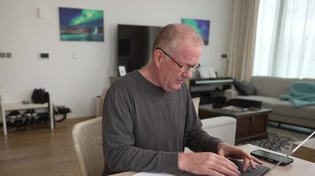 Frustrated senior man trying to fill out forms and organize paperwork on a laptop computer