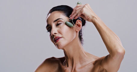 Beauty, facial and jade roller with woman in studio for antiaging cosmetics or dermatology. Gua...