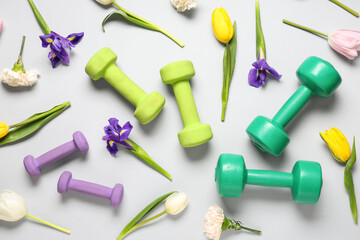 Composition with dumbbells and beautiful spring flowers on grey background