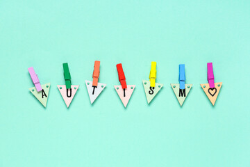 Word AUTISM made of wooden triangles with colorful clothespins on color background