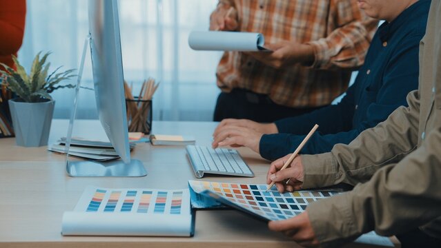 A diverse team works together in a modern office environment, selecting color palettes and designs while sharing ideas and resources for their creative project. SACTR