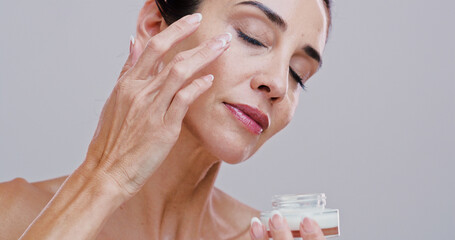 Skincare, mature woman and face cream in studio for anti aging treatment, wrinkle reduction and skin hydration. Space, person and beauty product application for self care wellness on white background