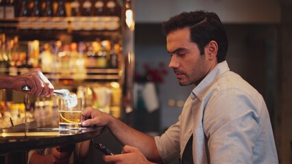 Smart man drinking cocktail in Old fashioned waiting friends or couple while chatting on smartphone to wait at counter bar with bartender preparing drinks at nightclub Friday meeting night. Vinosity.