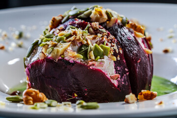 Beetroot with cottage cheese cream, nuts and pumpkin seeds on green spinach sauce is served on a white plate. Restaurant serving of a healthy dish. Close-up.