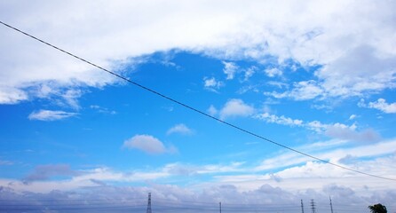 The sky is bright and beautiful blue, with white puffy clouds and electric cables running across it