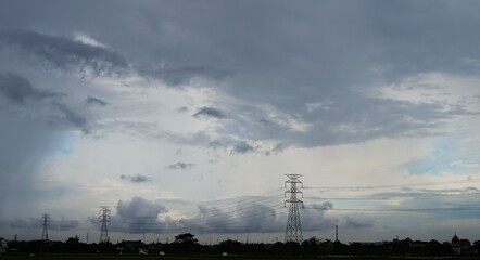 beautiful afternoon sky with black clouds indicating rain and electric towers and electric cables stretching
