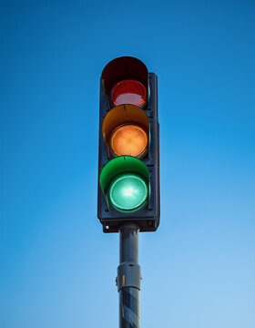 Traffic light standing against vivid blue sky, glowing red, orange and green lights. Minimalist shot