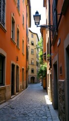 Fototapeta premium A picturesque alleyway, adorned with vibrant orange and soft beige buildings, invites exploration under the warm sunlight. The cobblestone path, flanked by lush greenery, creates a serene atmosphere