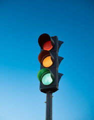 Traffic light standing against vivid blue sky, glowing red, orange and green lights. Minimalist shot