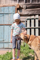 little girl is petting a big red dog in the village. girl in a headscarf is spending her summer in the countryside with a dog. 