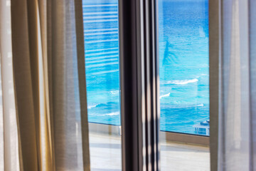Turquoise Caribbean Sea view through hotel window with sheer beige curtains in bright sunlight. Mexico.