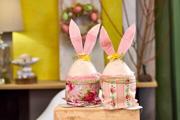 two handmade Easter bunnies made of eggs with pink ears stand on a table against a green wall