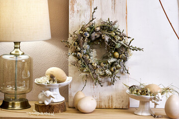 handmade Easter wreath made of natural materials, willow branches and quail eggs stands against a white wall in the interior © Vieille Prune