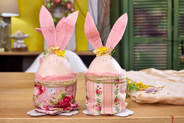 two handmade Easter bunnies made of eggs with pink ears stand on a table against a green wall