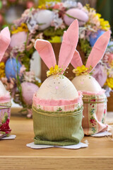 three handmade Easter bunnies made of eggs with pink ears stand on a table against a green wall