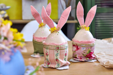three handmade Easter bunnies made of eggs with pink ears stand on a table against a green wall