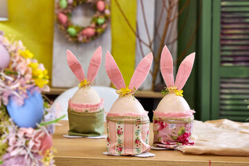 three handmade Easter bunnies made of eggs with pink ears stand on a table against a green wall