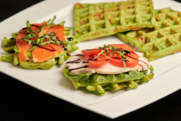 Belgian waffles with spinach on a white plate. Fish sandwiches, chicken sandwiches. Healthy eating. Close-up side view, isolated on black