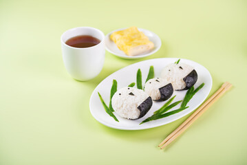 Rice ball onigiri with filling in the form of chicken with funny faces in a plate on a green background