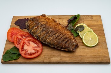 Served fried crucian carp on a wooden board. Fried fish with tomatoes, lemon and herbs