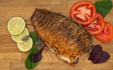 Served fried crucian carp on a wooden board. Fried fish with tomatoes, lemon and herbs