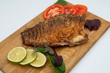 Served fried crucian carp on a wooden board. Fried fish with tomatoes, lemon and herbs