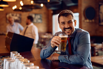 Happy businessman drinking beer in pub and looking at camera.