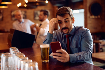 Distraught entrepreneur using mobile phone while sitting at bar counter.