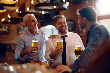 Happy male colleagues talking while drinking beer in pub after business meeting.