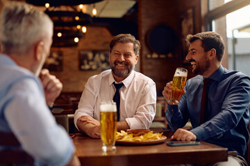 Happy businessman enjoying in beer and conversation with coworkers in pub.