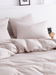 Bedroom with a double bed, fluffy down comforter, four pillows, wooden bedside table and alarm clock. Close-up side view vertical photo