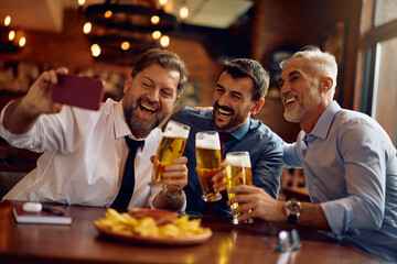 Cheerful business coworkers taking selfie while drinking beer in bar.