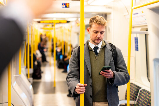 Businessman using smartphone while standing on subway train - Powered by Adobe