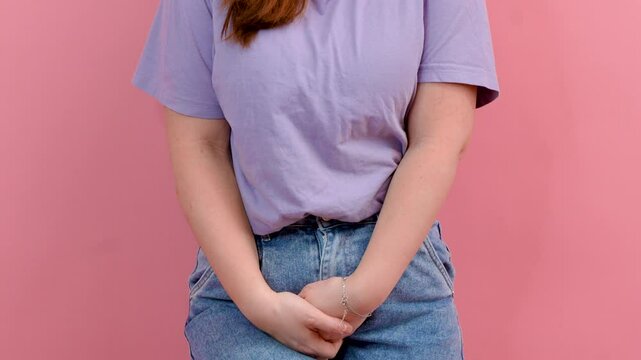 A young woman holds onto her perineum and wants to pee on an isolated background, the concept of urinary incontinence and urological diseases