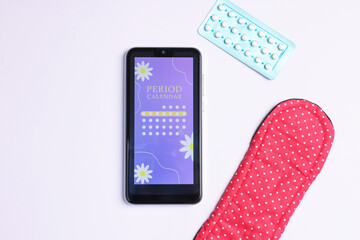 Smartphone with period calendar application and menstrual products on white background, flat lay