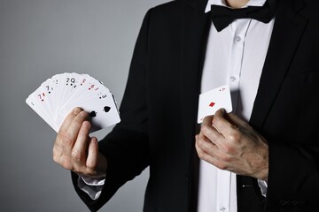 Illusionist hiding one playing card behind jacket lapel while showing deck on grey background,...